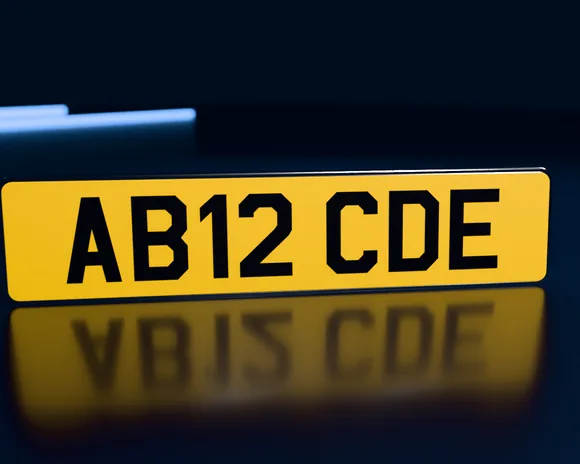 A standard 520 × 111mm yellow rear number plate reading AB12 CDE