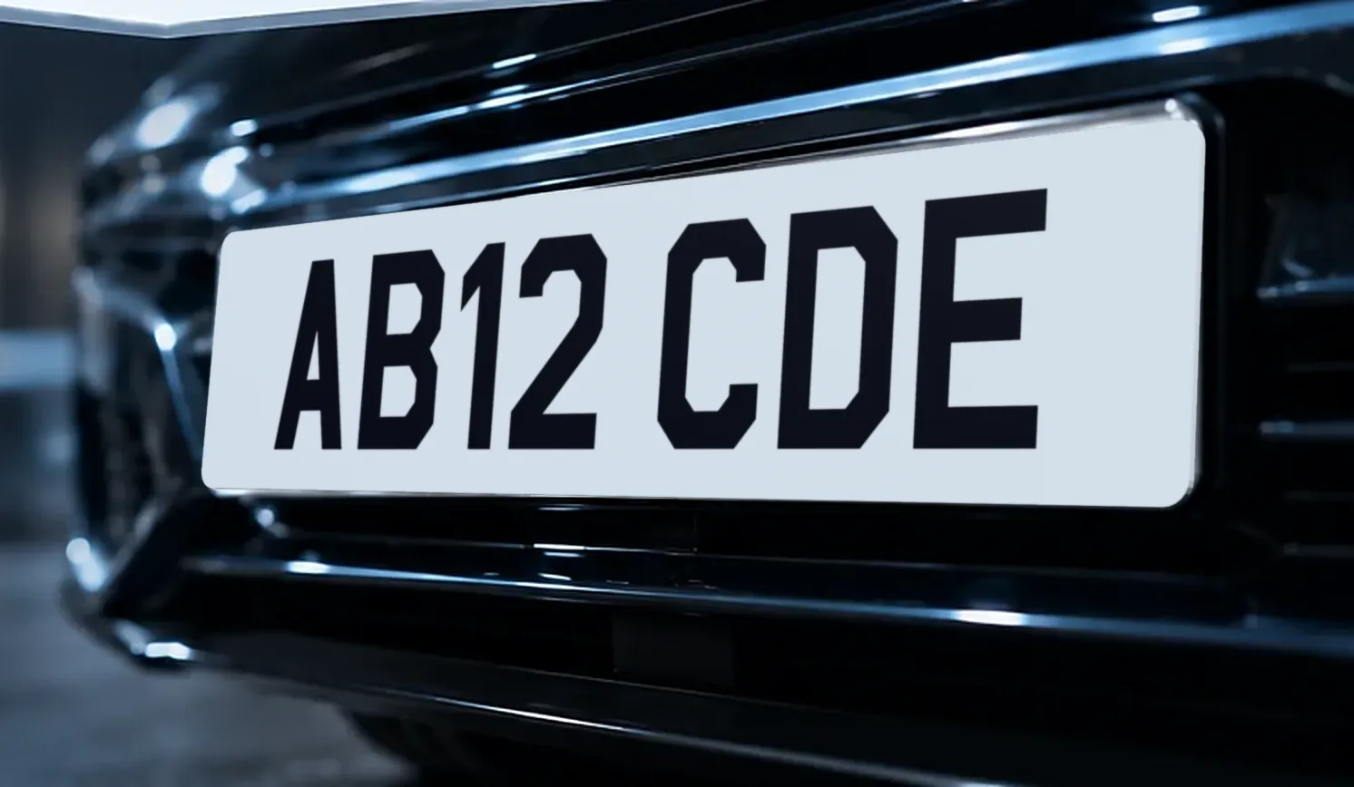 The front of a dark car fitted with a white oversized number plate